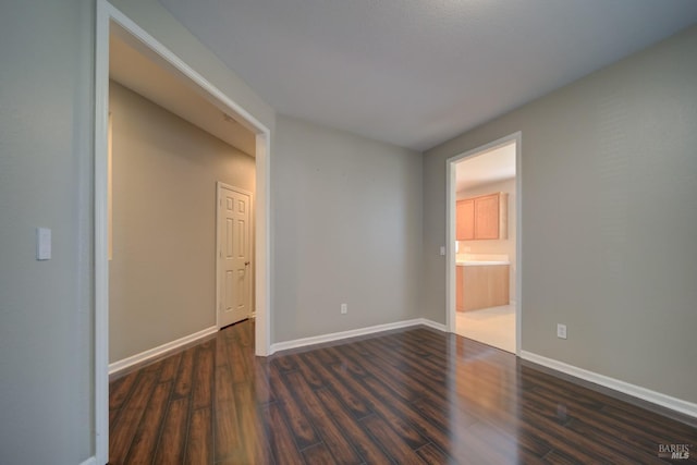 unfurnished bedroom with dark wood-style floors, baseboards, and ensuite bathroom