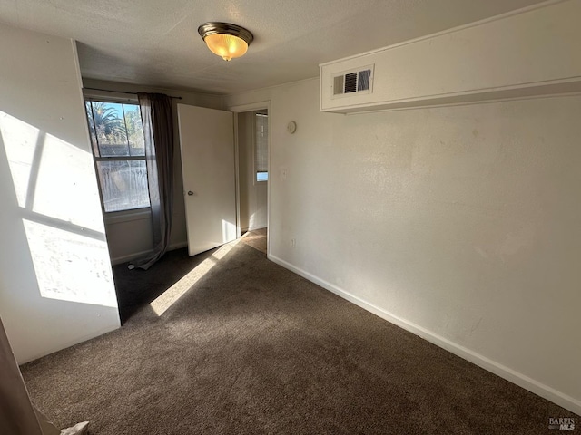 unfurnished room featuring visible vents, dark carpet, a textured ceiling, and baseboards