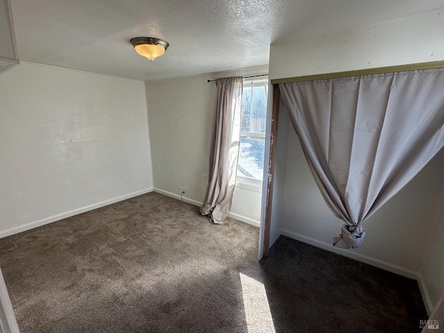 spare room with a textured ceiling, carpet, and baseboards