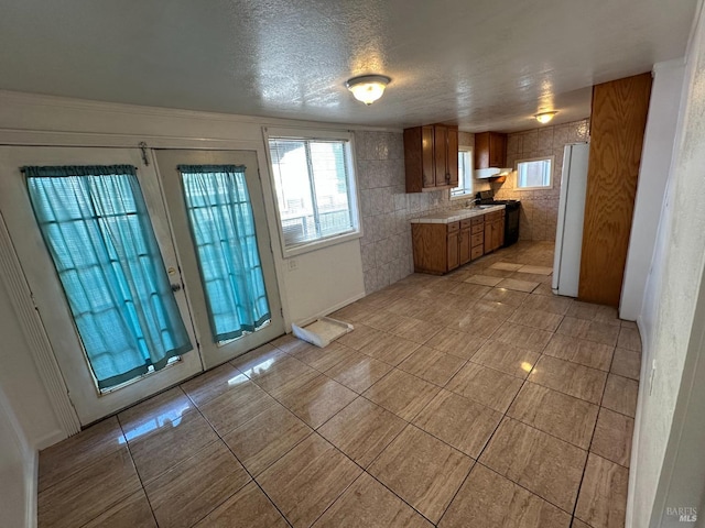 kitchen with french doors, brown cabinets, light countertops, freestanding refrigerator, and under cabinet range hood