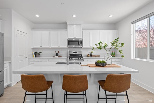 kitchen featuring a breakfast bar area, stainless steel appliances, light countertops, light wood-style floors, and white cabinetry