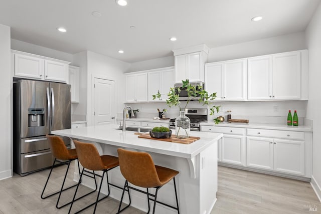 kitchen featuring white cabinets, an island with sink, appliances with stainless steel finishes, light countertops, and a sink