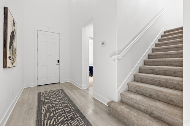 foyer entrance featuring stairs, light wood-type flooring, a towering ceiling, and baseboards