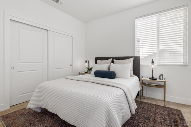 bedroom with a closet, light carpet, visible vents, and baseboards