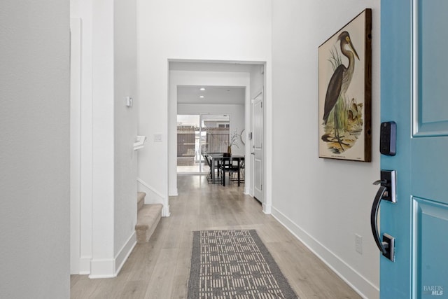 corridor featuring baseboards, light wood finished floors, and stairs