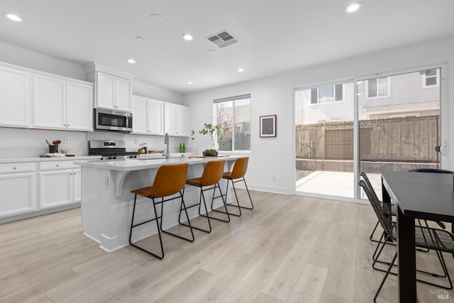 kitchen featuring a breakfast bar area, stainless steel appliances, visible vents, light wood finished floors, and an island with sink