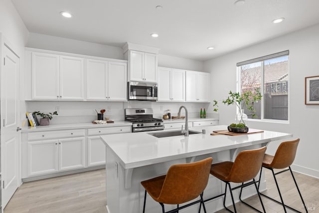 kitchen featuring stainless steel appliances, a sink, white cabinets, light countertops, and light wood-type flooring