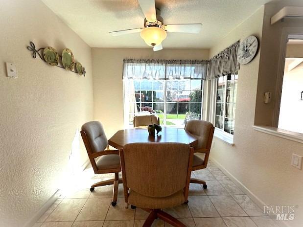 tiled dining area with a textured ceiling, a textured wall, a ceiling fan, and baseboards