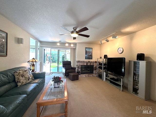 carpeted living area with lofted ceiling, rail lighting, a ceiling fan, a brick fireplace, and a textured ceiling