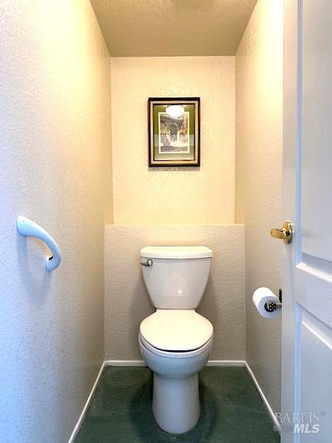 bathroom featuring toilet, baseboards, and a textured wall