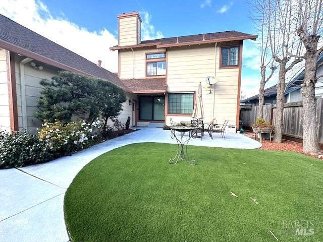 rear view of house with a patio area, a chimney, fence, and a yard