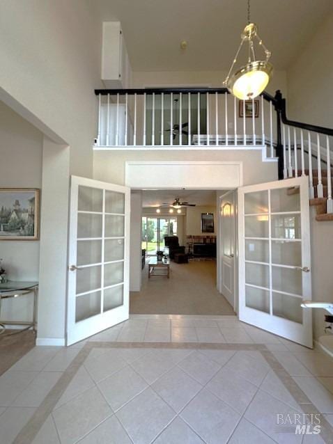 tiled entrance foyer with baseboards, ceiling fan, stairway, and a towering ceiling