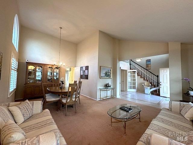 carpeted living room with high vaulted ceiling, stairway, and an inviting chandelier