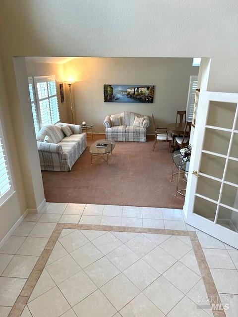 unfurnished living room featuring carpet, a textured ceiling, baseboards, and tile patterned floors