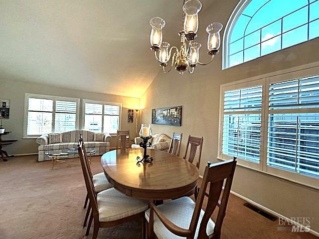 carpeted dining room featuring baseboards, high vaulted ceiling, visible vents, and a notable chandelier