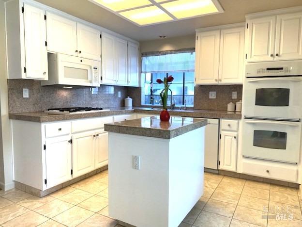 kitchen featuring white appliances, light tile patterned floors, a center island, white cabinetry, and a sink