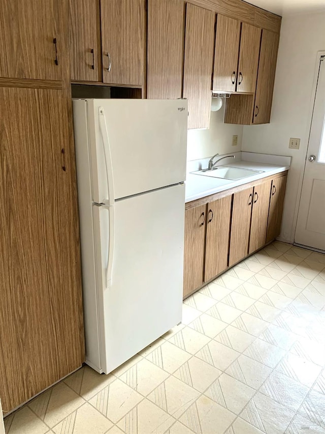 kitchen with freestanding refrigerator, light countertops, a sink, and light floors