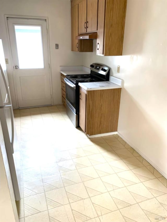 kitchen with light countertops, brown cabinetry, freestanding refrigerator, stainless steel range with electric cooktop, and under cabinet range hood