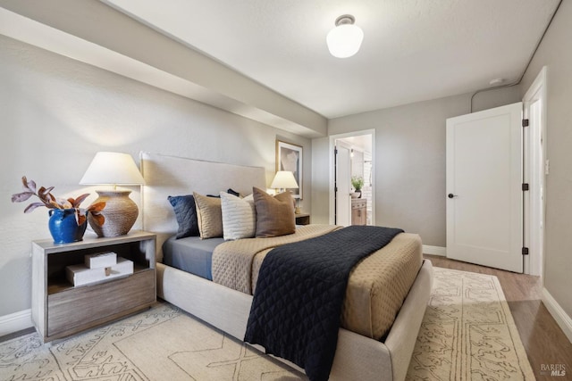 bedroom with ensuite bathroom, light wood finished floors, and baseboards