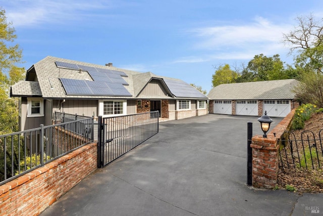 view of front facade with an outbuilding, fence private yard, a detached garage, a gate, and roof mounted solar panels