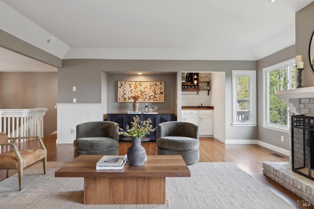 living area with light wood-type flooring, lofted ceiling, a brick fireplace, and indoor wet bar