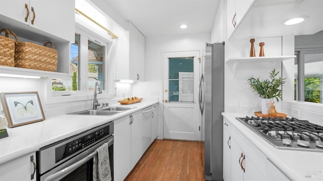 kitchen with stainless steel appliances, wood finished floors, a sink, white cabinetry, and light countertops