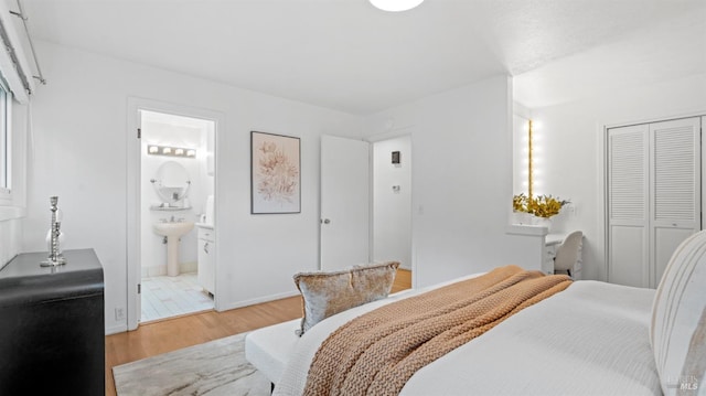 bedroom featuring light wood finished floors, a closet, ensuite bath, and baseboards