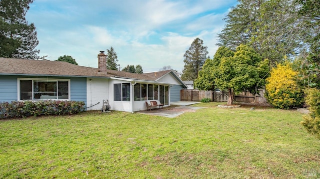 back of property featuring a lawn, a patio, a sunroom, a chimney, and fence