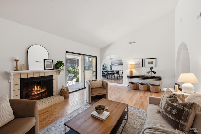 living area featuring arched walkways, high vaulted ceiling, a fireplace, wood finished floors, and visible vents