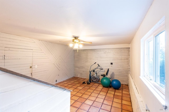 exercise room with ceiling fan and wooden walls