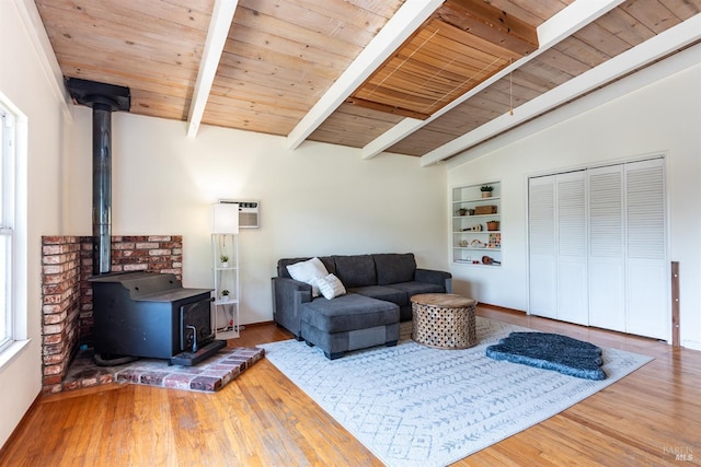 living room featuring lofted ceiling with beams, wood ceiling, wood finished floors, a wood stove, and a wall mounted AC