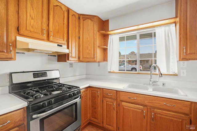 kitchen with brown cabinets, a sink, under cabinet range hood, and gas range