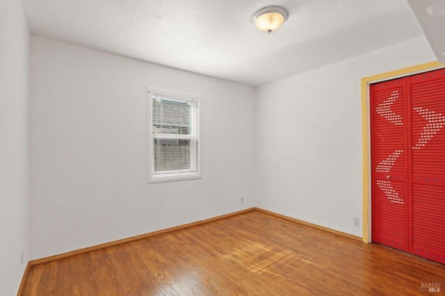 empty room with a textured ceiling, baseboards, and wood finished floors