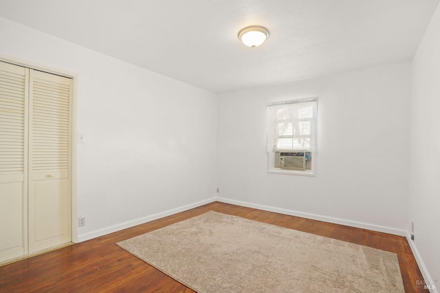 unfurnished bedroom featuring cooling unit, a closet, baseboards, and wood finished floors