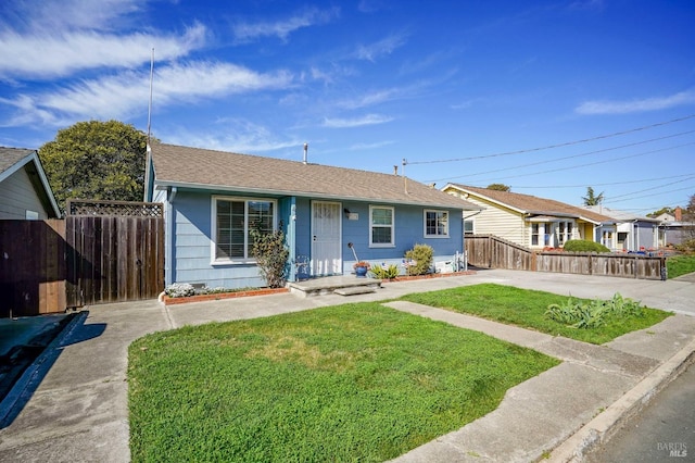 view of front of home featuring a shingled roof, fence, concrete driveway, and a front yard