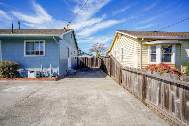 view of property exterior featuring driveway, a shingled roof, and fence