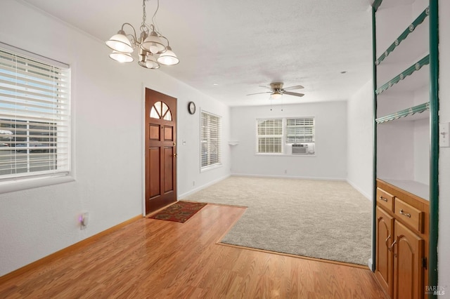 foyer entrance with light wood-style floors, light carpet, cooling unit, baseboards, and ceiling fan with notable chandelier