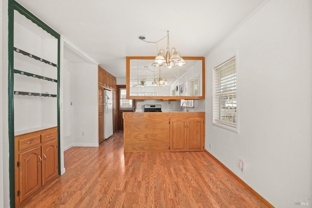 kitchen with stainless steel gas stove, freestanding refrigerator, a sink, light wood-type flooring, and a notable chandelier