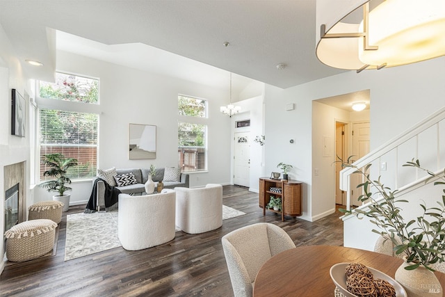 living room with dark wood finished floors, stairway, an inviting chandelier, a glass covered fireplace, and baseboards