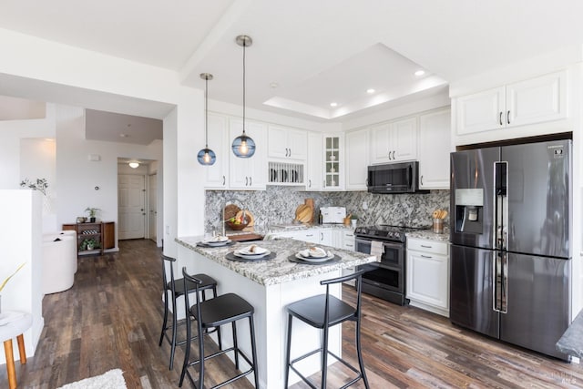 kitchen with a breakfast bar area, white cabinetry, appliances with stainless steel finishes, a tray ceiling, and tasteful backsplash