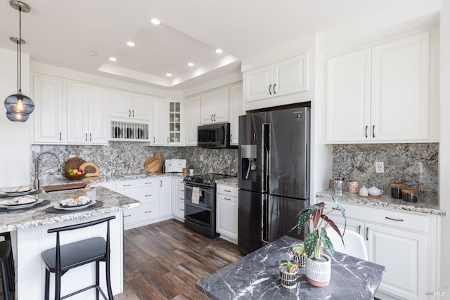 kitchen featuring white cabinets, a raised ceiling, light stone counters, dark wood-type flooring, and black appliances