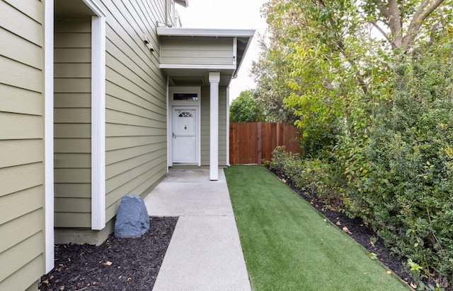 view of exterior entry with fence and a lawn