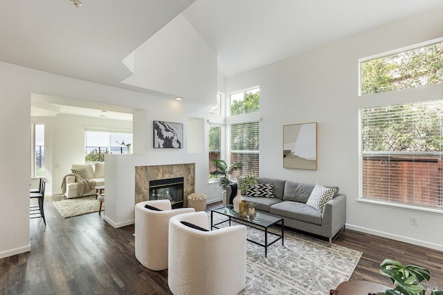 living area with a tile fireplace, dark wood-style flooring, a high ceiling, and baseboards