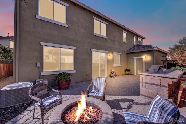 back of property at dusk featuring stucco siding, a patio area, a fire pit, and central AC unit