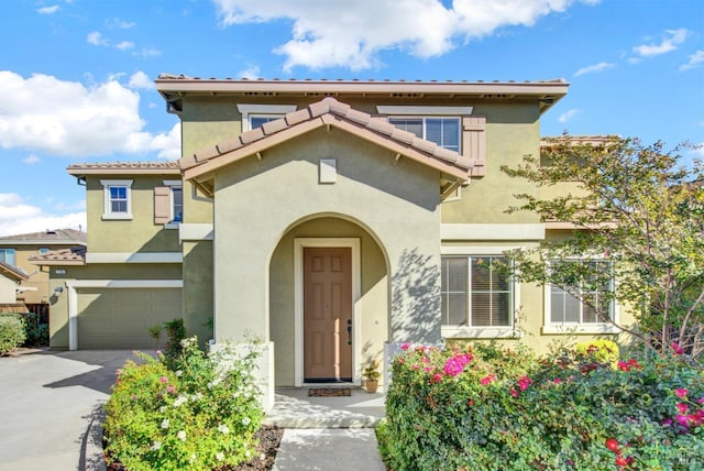 view of front facade featuring driveway, a tiled roof, an attached garage, and stucco siding