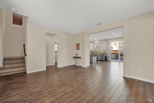 unfurnished living room with dark wood-style floors, stairs, visible vents, and baseboards