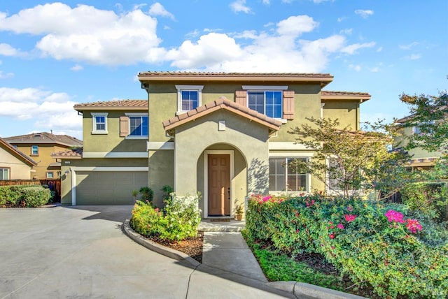 mediterranean / spanish-style house featuring driveway, a tiled roof, an attached garage, and stucco siding