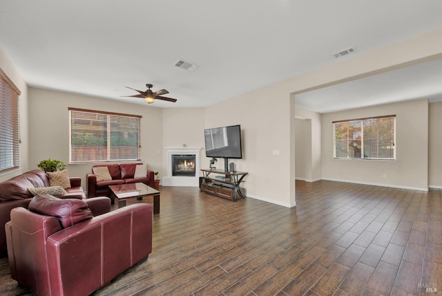 living room featuring dark wood-type flooring, a glass covered fireplace, visible vents, and baseboards