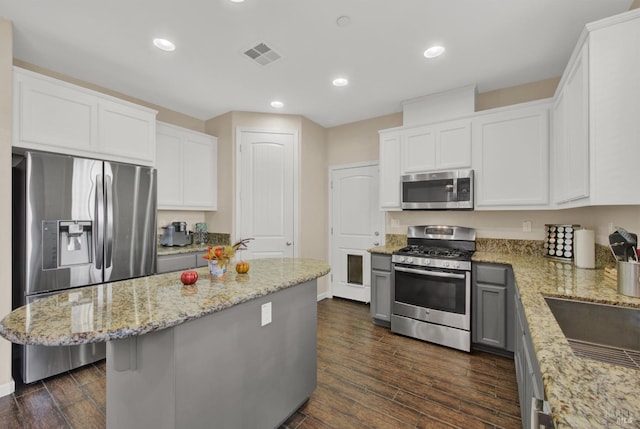 kitchen with dark wood-style floors, a center island, stainless steel appliances, visible vents, and light stone countertops