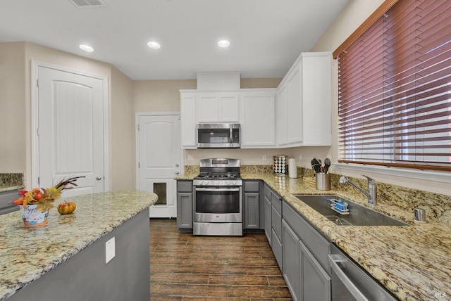 kitchen featuring stainless steel appliances, gray cabinets, dark wood-type flooring, a sink, and light stone countertops